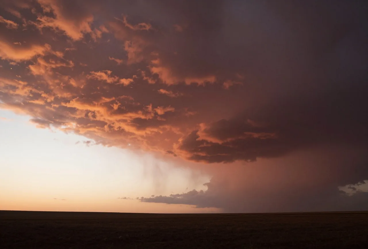 Dunkle Gewitterwolken über einer weiten Ebene in der Dämmerung, am Horizont ein heller Lichtstreifen