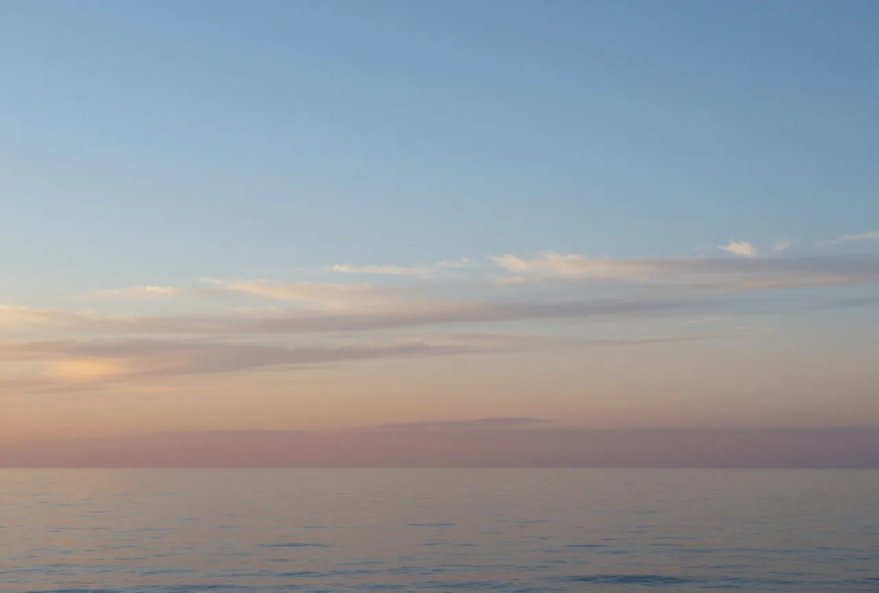 Klarer Morgenhimmel über einem ruhigen Meer mit zarten Wolkenschichten und weitem Horizont in Blau und Gold