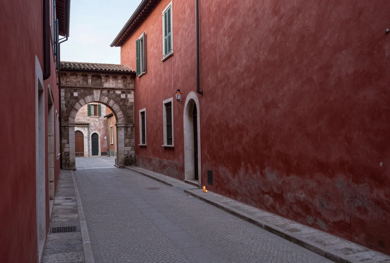 Eine schmale gepflasterte Gasse in einer antiken römischen Stadt mit verputzten Steinhäusern und einem kleinen Torbogen im Morgenlicht