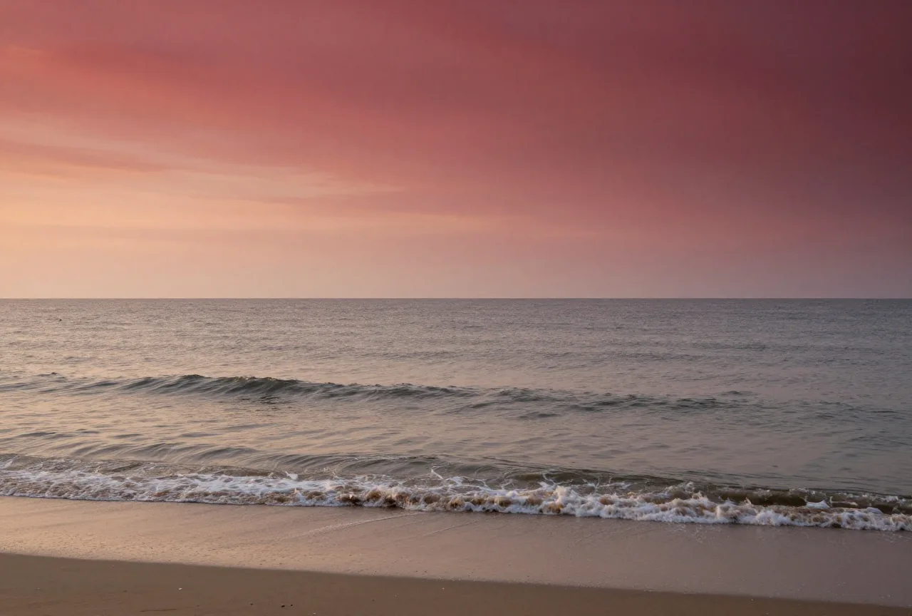 Ein weites Meeresufer mit Wind über flachem Wasser und nassem Sand unter bewegtem Himmel im Morgengrauen