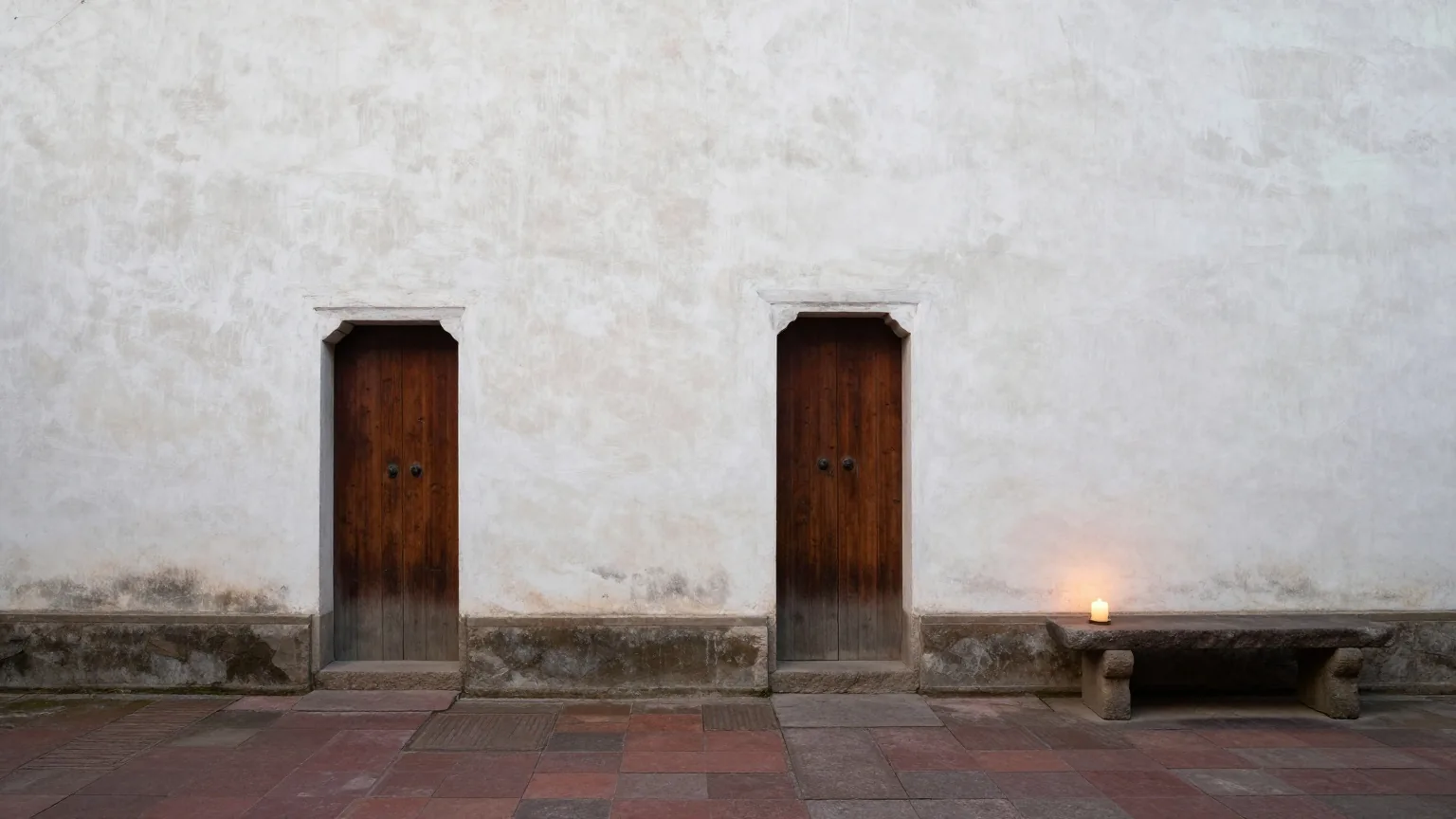 Der Innenhof eines einfachen antiken Hauses mit weiß gekalkten Wänden, halb offener Holztür und Steinbank im Nachmittagslicht