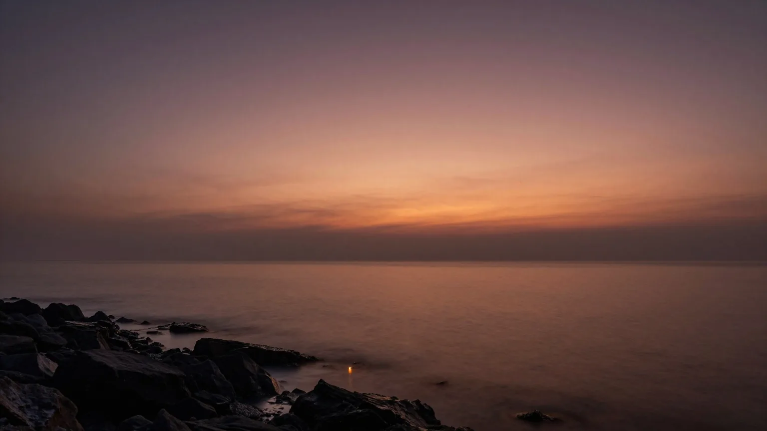 Erstes Morgenlicht über einem ruhigen dunklen Meer und einer felsigen Küste, Nebel liegt über dem Wasser